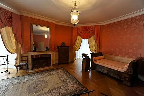 Chambre à coucher avec cheminée meublée d'un lit de travers à deux dossiers incurvés.