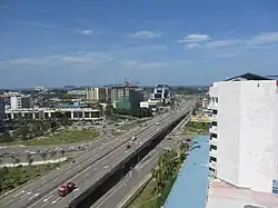 Photographie d'une route à trois voies traversant une ville moderne et tropicale.