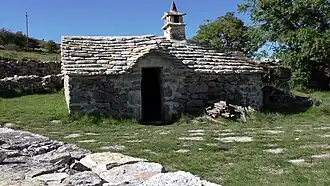 Cette cabane pastorale caussenarde utilise la voûte pour supporter le toit composé de lauzes et d'une cheminée coiffée de dalles de calcaire reposant sur des petites pierres verticales, surmontées d'une pierre conique appelée cocut.