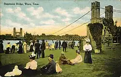Carte postale dépeignant en couleur des habitants devant le pont suspendu de Waco.