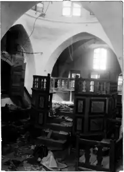 Photo d'archive en noir et blanc de l'intérieur d'une synagogue, avec au sol des traces de saccage.
