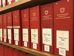 Photographie de plusieurs classeurs rouges avec étiquette blanche sur une étagère