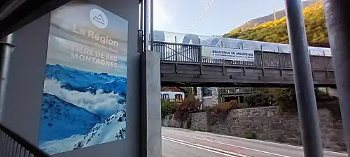 Photographie d'un panneau de soutien de la Région avec la passerelle de Francoz qui enjambe la route départementale 1006.