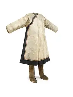 Manteau en peau de saumon de coupe chinoise avec fermeture asymétrique et passementerie en peau de poisson noire et rouge. Bottes en peau de renne, côté poil vers l'intérieur. Le côté chair est teint en brun, et la bordure est en tissu brun, rouge et noir. Peuple nivkh.