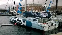 Vu de trois quarts arrière, voilier bleu sombre et bleu clair amarré au ponton