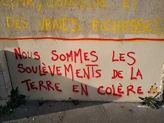 Texte peint en rouge sur un mur en majuscules, "Nous sommes les Soulèvements de la Terre".