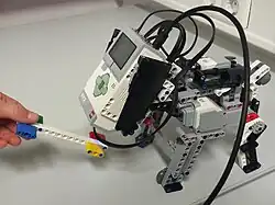 Photo d'un robot Mindstorms EV3 en action. Il ressemble à un petit chien. Sa brique moteur remplace sa tête.