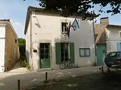 Photographie de la mairie de Talmont, petit bâtiment de style saintongeais abrité d'un tilleul et entouré de roses trémières