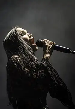 Une femme brune habillée d'un vêtement en dentelle noir chante dans un micro