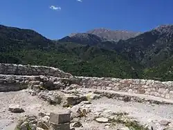 photographie couleurs : un mur de pierres au premier plan ; un paysage de montagnes boisées au fon
