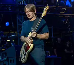 Chaney, aged 52, holds his guitar firmly. He wears a blue T-shirt and blue pants.