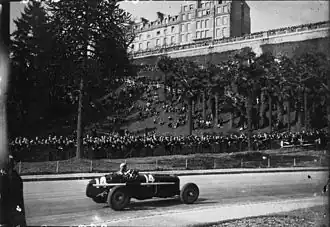 Photographie en noir-et-blanc d'une monoplace dans les rues d'une ville.