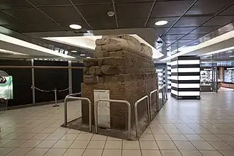 Photographie en couleurs d'un mur de pierres ancien dans un hall commercial.