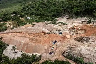 Photographie couleur aérienne d'une zone déboisée et excavée au milieu d'une forêt équatoriale.