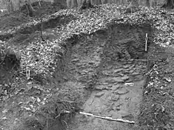 Photo en noir et blanc d'une fosse dont le sol est jonché de débris de tuiles.