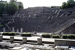 Photo des restes d'un amphithéâtre romain, avec des visiteurs assis sur les marches.