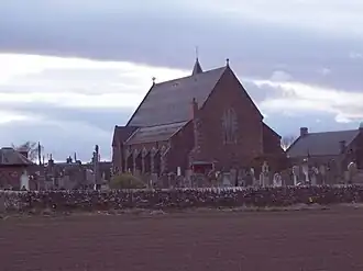 Église de grès rose et de style néogothique bâtie au milieu d'un cimetière.