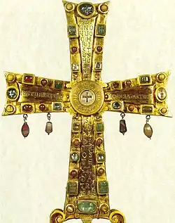 Photographie d'une croix dorée sertie de bijoux.