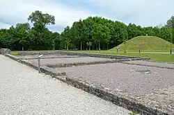 Vue générale de ruines avec un tumulus à l'arrière-plan.