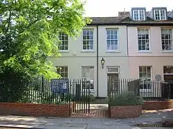 Bâtiment sur deux étages comportant de nombreuses fenêtres derrière une petite cour protégée par une grille.