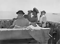 Photo en noir et blanc de trois hommes dont l'un est au téléphone et l'autre regarde dans des jumelles