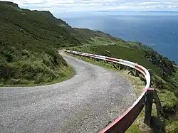 Photographie d'une route sinueuse bordée d'une glissière de sécurité la séparant d'une falaise au-dessus de la mer.