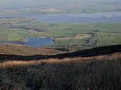 Pentes d'une montagne vues du sommet, et suivies d'une étendue d'eau en arrière-plan.