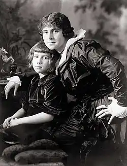 Photographie noir et blanc d'une femme blanche qui tient contre elle une petite fille. Elles portent des robes élégantes