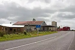 Quelques bâtiments bas au bord d'une route avec un panneau représentant une pompe à essence et le texte.