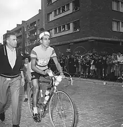 Photographie en noir et blanc montrant un cycliste sur son vélo, un homme se tenant à côté.