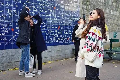 Touristes se prenant en photo devant le mur, formant un cœur avec les bras.