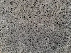 vue rapproché d'une pierre volcanique noire taillé. On y distingue les alvéoles de 0.5mm a 1mm.