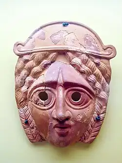  Visage de femme, yeux écarquillés, fronçant verticalement le front, cheveux ondulés tressés couverts d’une calotte.