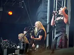 Quatre membres d'un groupe de rock, trois hommes et une femme, jouant sur scène.