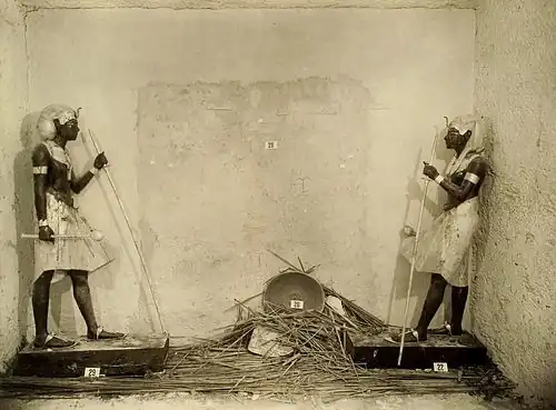 Statues noires royales encadrant un mur qui porte les traces d'une porte scellée menant à la chambre funéraire.