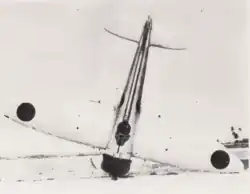 Photo noir et blanc d'un avion dressé à la verticale sur son nez et en équilibre précaire sur la pointe de l'une de ses ailes.