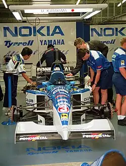 Vue d'une monoplace bleue et blanche devant un garage.