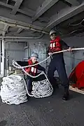 Marin de la Marine américaine lovant un cordage d’amarre du croiseur USS&nbsp;Philippine&nbsp;Sea.