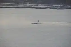 Photo de l'avion sur le fleuve, au centre de l'image, juste après l'amerrissage, avec la ville en arrière-plan.