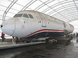 Photo de l'avant du corps de l'avion, dans un grand hangar, avec des traces de boues et d'impact d'oiseaux visibles, notamment avec un trou sur son nez.