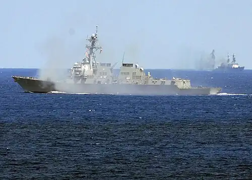 L'USS&nbsp;Oscar Austin faisant feu contre la cible (au fond).