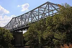 Vue d'un pont métallique enjambant un cours d'eau. Des arbres sont présents de part et d'autre.