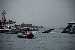 L'avion, au centre de l'image, à peine visible à mesure qu'il coule dans le fleuve, est entouré par plusieurs navires de secours.
