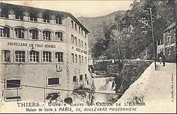 Vieille photographie de l'usine prise avec une toile pendue à une fenêtre du 1er étage où un premier diable rouge est peint au début du XXe siècle.