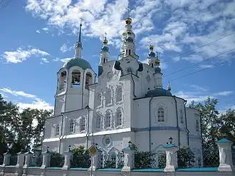 Photographie en contre-plongée d'un bâtiment religieux de type cathédral blanc avec des toits bleus où se trouvent des croix orthodoxes.