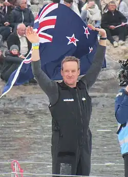 Faisant flotter un drapeau néo-zélandais, le navigateur salue la foule.