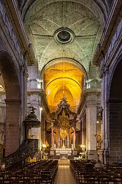 Photographie du vaisseau central de l'église, prise depuis l'entrée. Le chœur est brillamment éclairé.