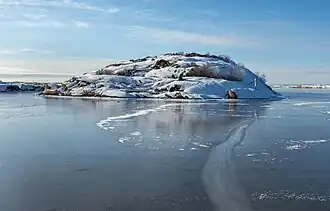 L'île de Vassholmen en sortant du port de Väjern, à Kungshamm. À l'intérieur de cette baie abritée, la glace s'est formée pendant les jours calmes, la rendant claire et "noire". Le panneau de signalisation est l'un des nombreux qui se trouvent le long de la côte suédoise. Les petites "croix" sont d'anciens dispositifs d'amarrage (une sorte de bollards ou de taquets) du début du 20e siècle. Février 2021.