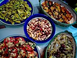 La phtographie couleur montre un assortiment de cinq bols et plats garnis de hors-d'œuvre variés : tomate, olives, courgettes, poivrons... Tous les plats ne sont pas identifiables.