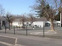 Photographie en couleurs d'une cours avec des dessins au sol ; long bâtiment largement vitré en arrière-plan.